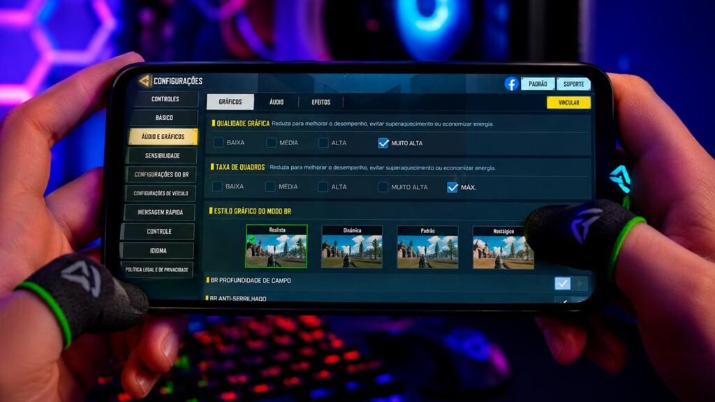 Tela de configurações gráficas de um jogo de mundo aberto exibida em um smartphone gamer moderno. A interface apresenta opções de qualidade visual, taxa de quadros (FPS), efeitos gráficos e resolução, permitindo ao jogador personalizar o desempenho do jogo. Ao fundo, um ambiente gamer com iluminação RGB reforça a atmosfera tecnológica e destaca a evolução dos jogos mobile em termos de gráficos e personalização