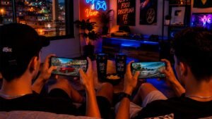 A imagem mostra duas pessoas sentadas em um sofá jogando um jogo multiplayer de carros rebaixados em seus smartphones. Cada celular exibe um carro personalizado em um mapa urbano inspirado no Brasil, enquanto o ambiente gamer conta com iluminação RGB, decoração moderna e uma vista noturna, transmitindo uma atmosfera descontraída e imersiva para partidas online entre amigos